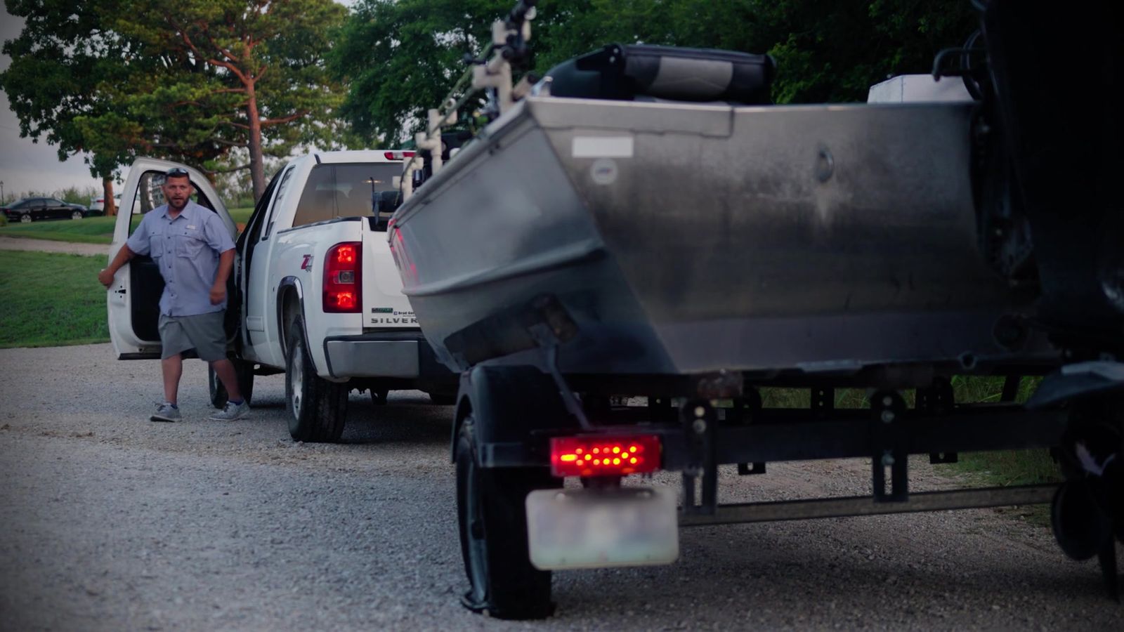 A pickup pulling a boat trailer stopped on a gravel lot with the owner walking back to the trailer